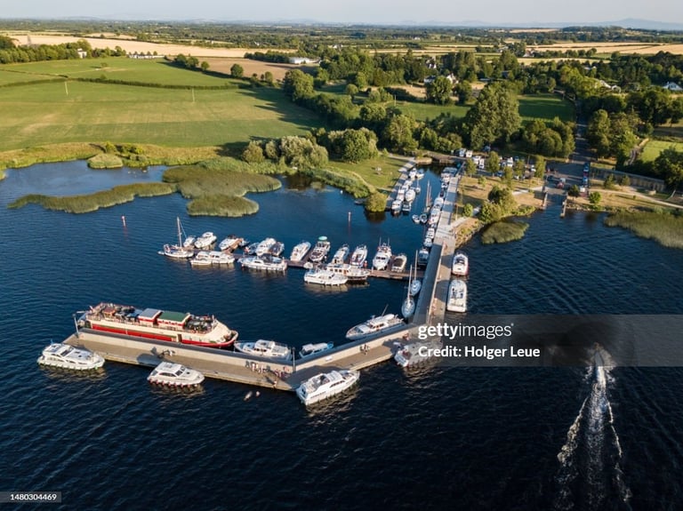 Aerial view of a marina with moored boats, a large cargo ship, and surrounding green farmland and waterways