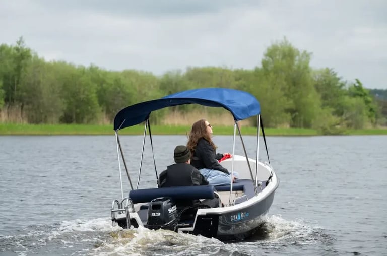 Two people in a small motorboat with blue canopy driving on water with trees in background